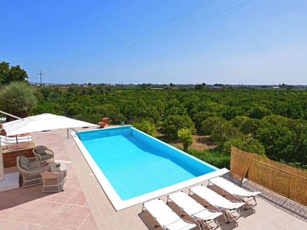 Une piscine rectangulaire bordée de blanc, entourée de chaises longues et d’une table.