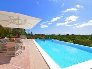 Une piscine avec vue sur la campagne, entourée de mobilier d’extérieur et d’un grand parasol.