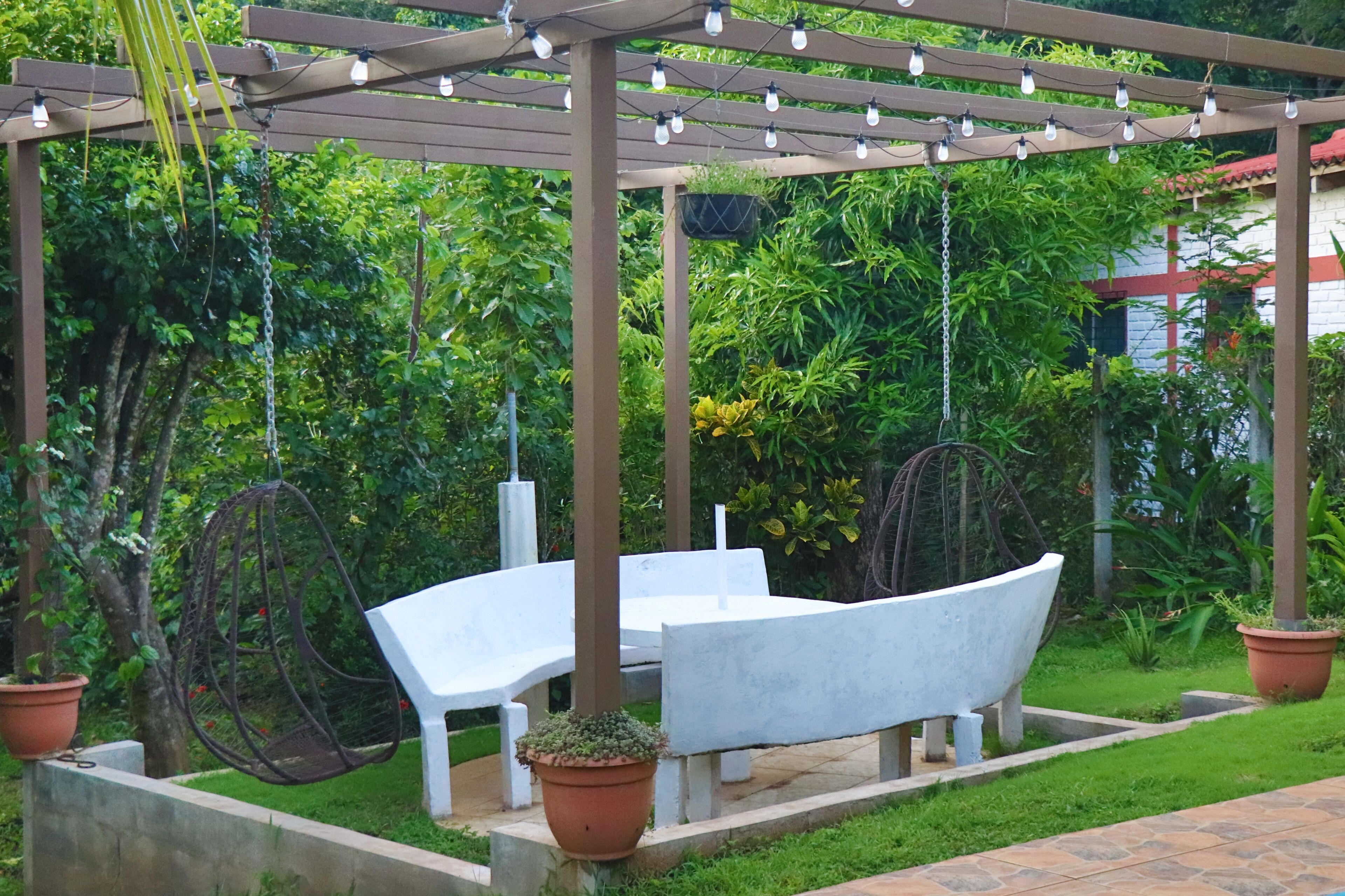 Eine Gartenpatio mit einer Pergola, Hängestühlen und einem weißen Tisch.