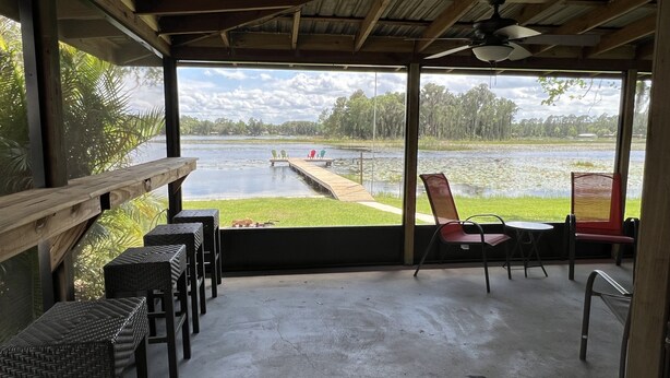 A covered outdoor seating area with a view of a lake and dock. - Lakeside Retreat with Dock/Porch/Firepit/Beach (Fort McCoy)