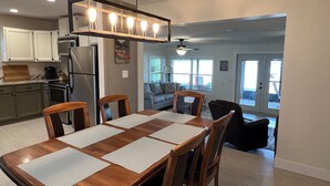 A modern kitchen with white cabinets, a stainless steel refrigerator, and a dining area with a wooden table and chairs. - Lakeside Retreat with Dock/Porch/Firepit/Beach (Fort McCoy)