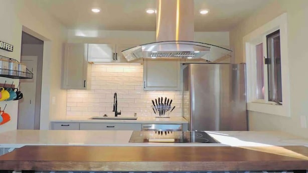 A modern kitchen with a central island, stainless steel appliances, and a glass-fronted range hood. - Modern getaway! Relax, bike, hike, and shred! (Angel Fire)