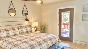 A bedroom with a bed, a bench, a ceiling fan, two wall mirrors, a nightstand with a lamp, and a door leading to a balcony. - Modern getaway! Relax, bike, hike, and shred! (Angel Fire)