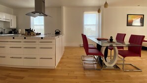 A modern kitchen with white cabinetry, a large island, and a dining area with red chairs and a glass table. - Spacious 2 br apartment in the heart of Montreal (Montréal)