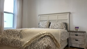 A neatly made bed with patterned bedding, a bedside table with a clock, and a window with curtains. - Spacious 2 br apartment in the heart of Montreal (Montréal)