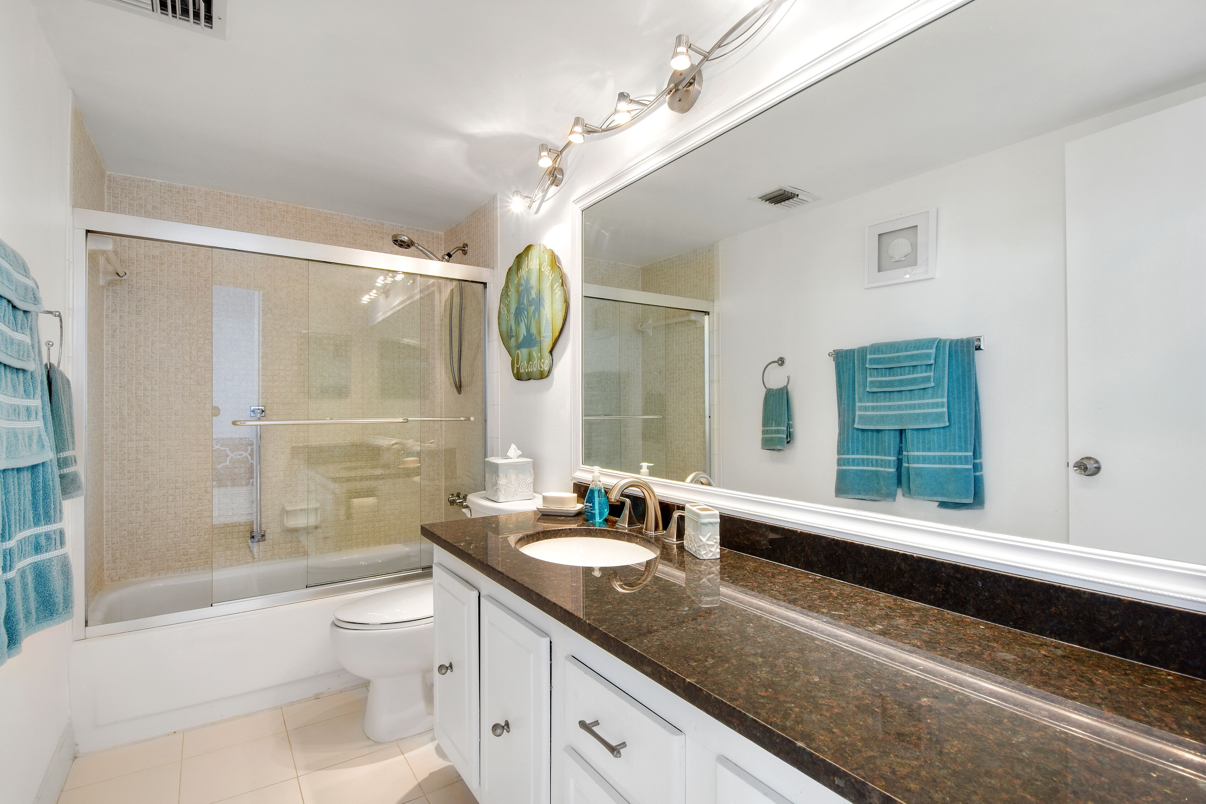 A modern bathroom with a glass-enclosed shower, a white toilet, a sink with a granite countertop, and a large mirror.