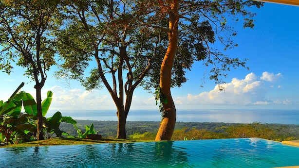 Une piscine à débordement offrant une vue sur l’océan et les collines lointaines.