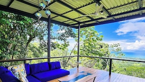 Un espace extérieur aménagé avec des meubles de jardin, comprenant des canapés bleus et une table basse en bois, et offrant une vue sur un paysage verdoyant.