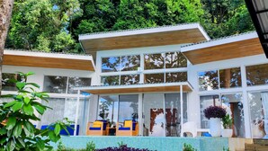 Une maison moderne dotée de grandes fenêtres, d’un balcon et d’un jardin.