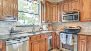 A kitchen with wooden cabinets, stainless steel appliances, a window, and a stone backsplash. - Dock & Game Room: Alvarado Lake Getaway! (Alvarado)