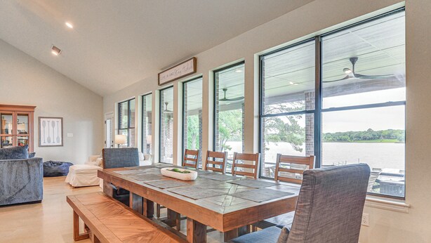 A spacious dining area with a large wooden table, comfortable seating, and large windows offering a view of the outdoors. - Dock & Game Room: Alvarado Lake Getaway! (Alvarado)