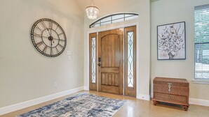 A hallway with a wooden door, a wall clock, a framed artwork, and a wicker chest of drawers. - Dock & Game Room: Alvarado Lake Getaway! (Alvarado)
