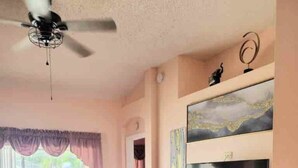 A spacious living room with a large TV, a ceiling fan, and a view of a pool through the glass door. - Relaxing 3 Bedroom Pool Home (Tampa)