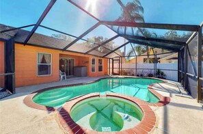 A swimming pool with a glass enclosure, a patio area, and a house with a red exterior. - Relaxing 3 Bedroom Pool Home (Tampa)