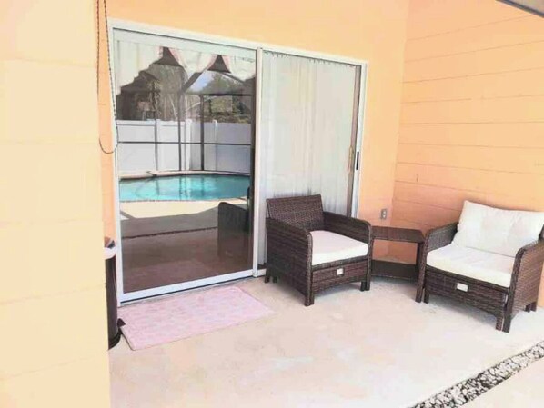 A patio area with a sliding glass door leading to a pool, two wicker chairs, and a small rug. - Relaxing 3 Bedroom Pool Home (Tampa)