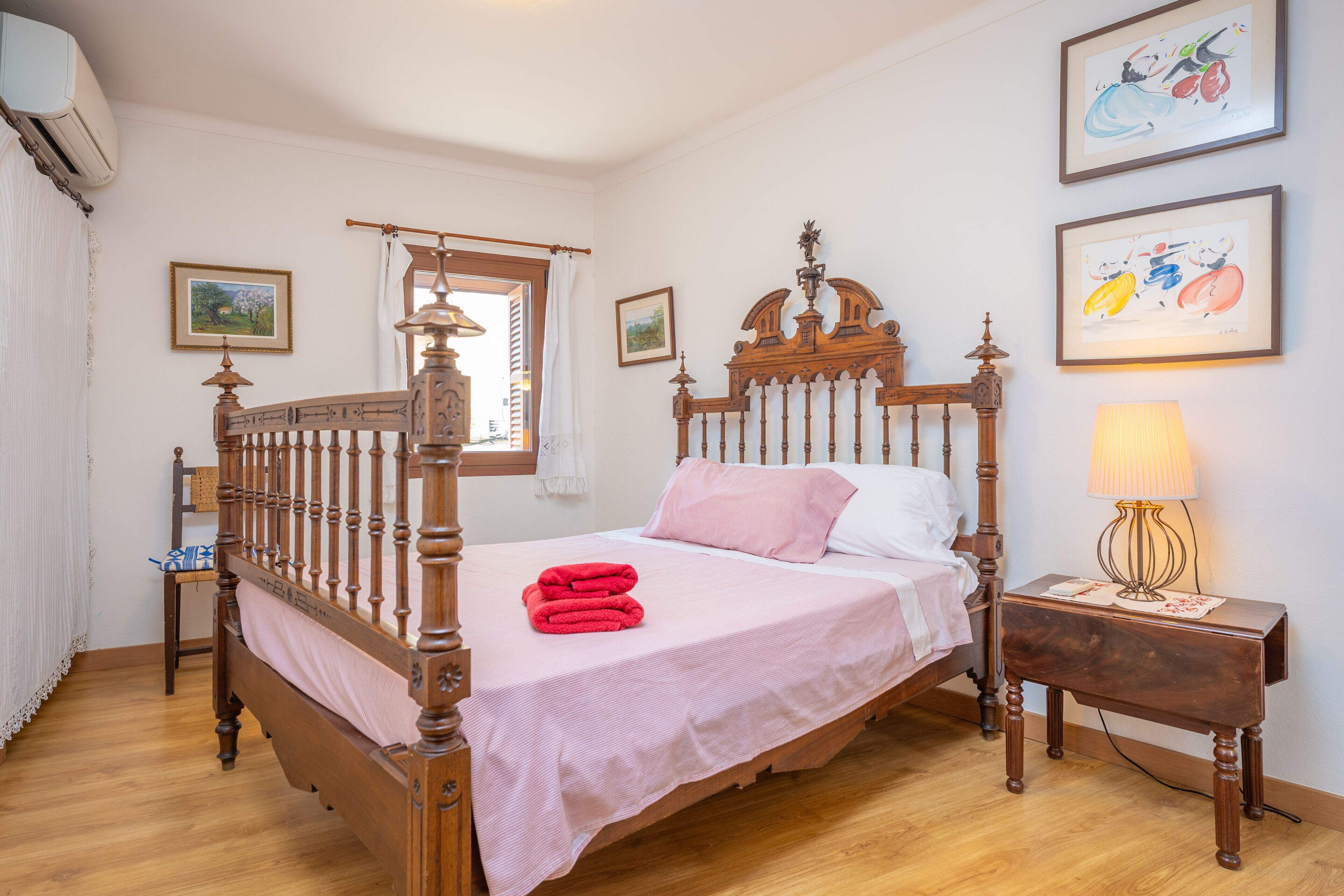 A bedroom with a wooden four-poster bed, a bedside table with a lamp, and two framed pictures on the wall.