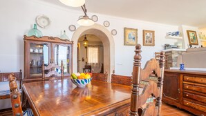 A dining area with a wooden table, chairs, and a bowl of fruit. There is a cabinet with glass doors and a chandelier above the table. - CAN VIDAL - Cozy House with Private Pool and Free WiFi (Campanet)