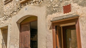 A stone building with a wooden door and window shutters, a visible number '74' on the wall, and a small window with a metal grille. - CAN VIDAL - Cozy House with Private Pool and Free WiFi (Campanet)
