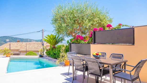 A swimming pool with a table and chairs, surrounded by greenery and a view of the hills. - CAN VIDAL - Cozy House with Private Pool and Free WiFi (Campanet)