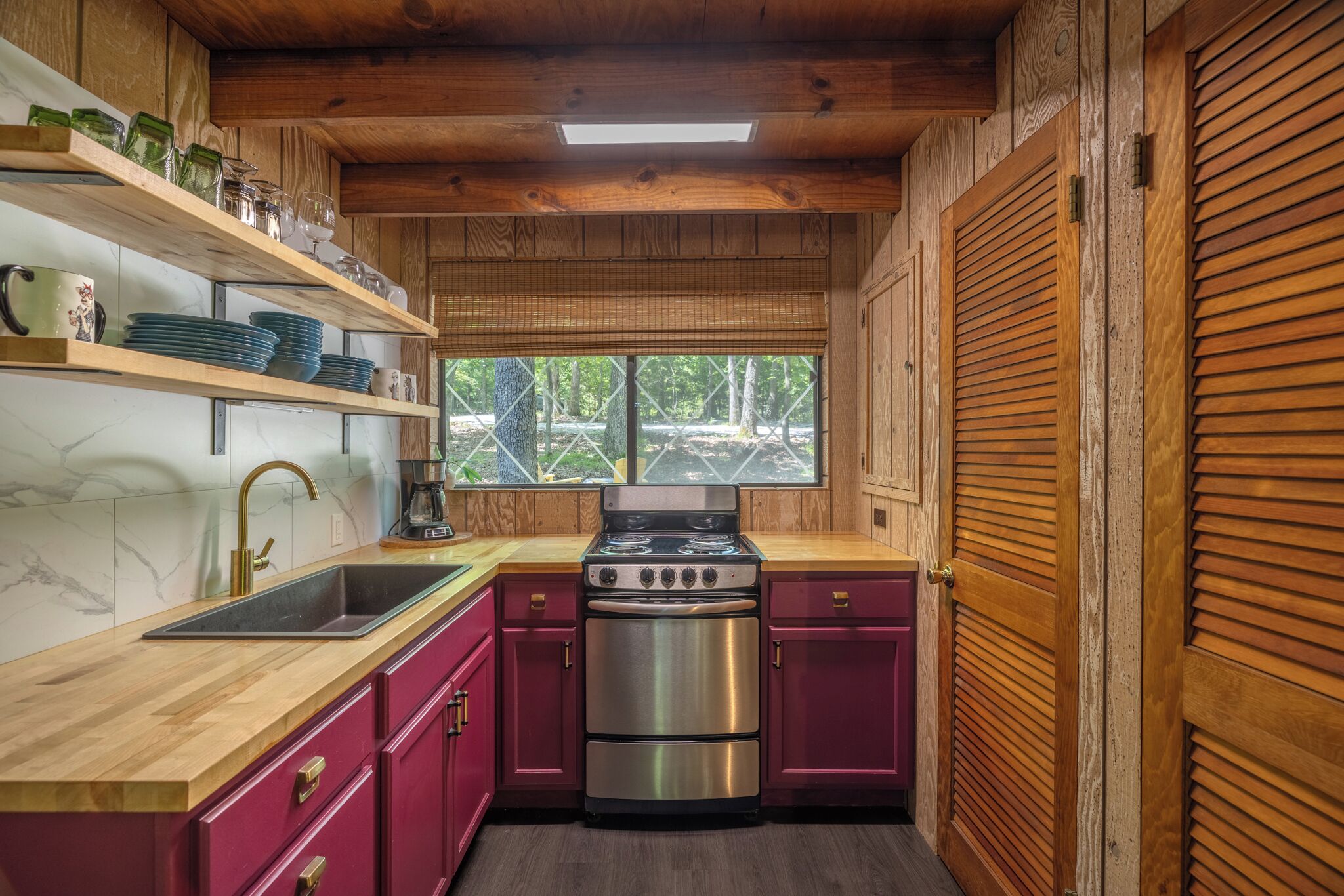 A kitchen with wooden cabinets, a stainless steel stove, and a window overlooking a wooded area.