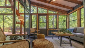 A cozy interior with large windows, wicker furniture, and a wooden table. - The Cocoon Chalet by Innsbrook Vacations! (Innsbrook)