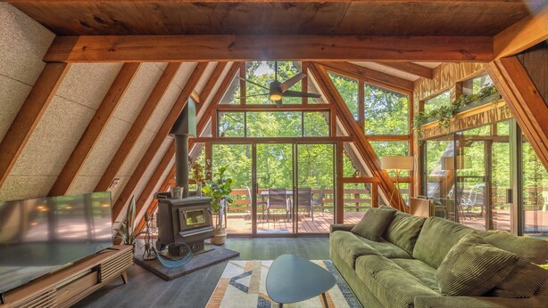 A cozy attic room with a large window, a fireplace, and a green sofa. - The Cocoon Chalet by Innsbrook Vacations! (Innsbrook)