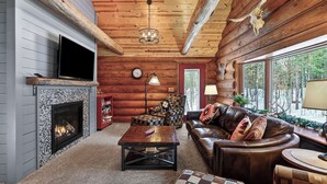 A log cabin interior with a fireplace, leather sofa, patterned armchair, and a view of the outdoors. - Family Log Cabin - Lake, Golf, Pool, Hike, Ski-ATV & Game Room - Northwoods WI (Danbury)