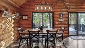A log cabin interior with a dining table, chairs, a chandelier, and a view of the forest through large windows. - Family Log Cabin - Lake, Golf, Pool, Hike, Ski-ATV & Game Room - Northwoods WI (Danbury)