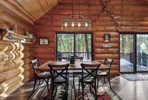 A log cabin interior with a dining table, chairs, a chandelier, and a view of the forest through large windows. - Family Log Cabin - Lake, Golf, Pool, Hike, Ski-ATV & Game Room - Northwoods WI (Danbury)