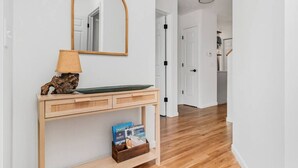 Un pasillo con una consola de madera, un espejo, una lámpara y una cesta pequeña con libros.