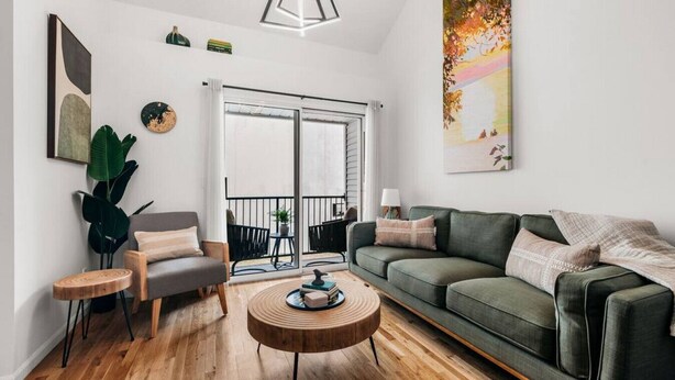 Una sala de estar moderna con un sofá verde, un sillón gris, una mesa de centro de madera y un ventanal con vistas al exterior.