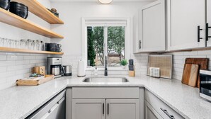 Cocina moderna con muebles blancos, encimera de granito, lavavajillas integrado y ventana con vista a zonas verdes.