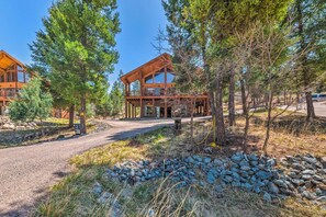 A lodge with a large wooden structure, a covered deck, and a gravel driveway surrounded by trees and rocks.
