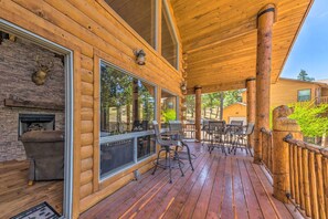 A wooden deck with outdoor furniture, a stone fireplace, and large windows overlooking a forested area. - Quiet Ruidoso Cabin w/ Deck & Private Hot Tub (Ruidoso)