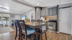 Une cuisine moderne dotée d’appareils électroménagers en acier inoxydable, un coin repas avec des chaises en bois et une grande fenêtre donnant sur un jardin.