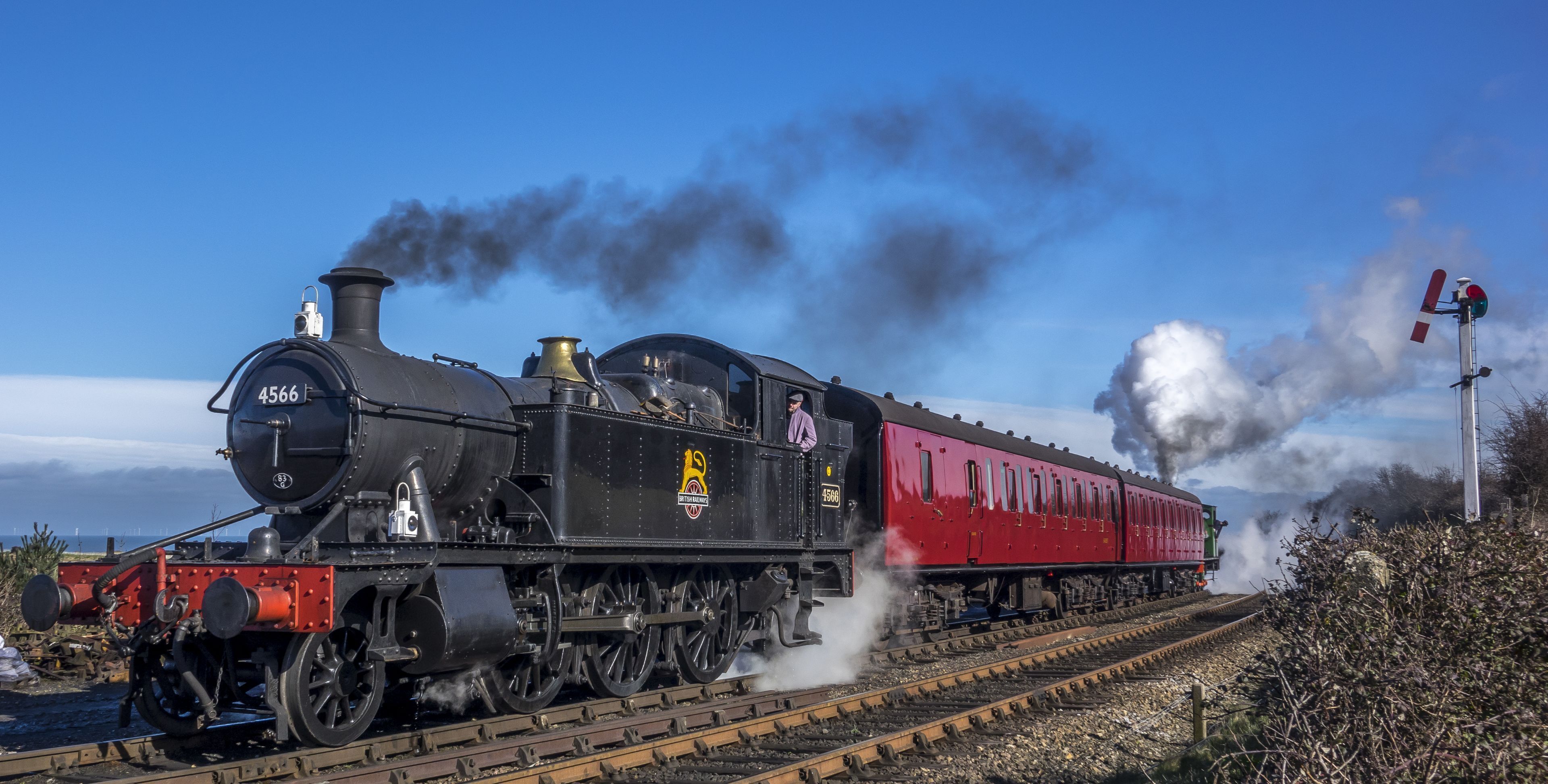 Une locomotive à vapeur portant le numéro 4566 à l’avant, tirant un wagon de voyageurs rouge.