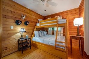 Habitación con literas, paredes de madera, ventilador de techo, una lámpara y dos sombreros en la pared.
