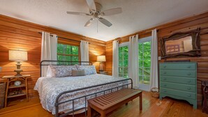 Een houten slaapkamer met een bed, nachtkastjes, een bankje, een dressoir en een plafondventilator.