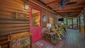 Een chalet met een rode deur, houten wanden, een veranda met stoelen en een plafondventilator.