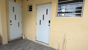 Un edificio con dos puertas blancas, una ventana con persianas horizontales y un piso de baldosas.