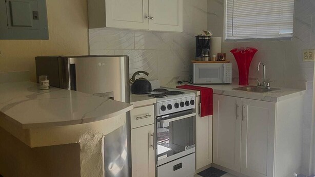Cocina compacta con estufa, microondas y una tetera roja.