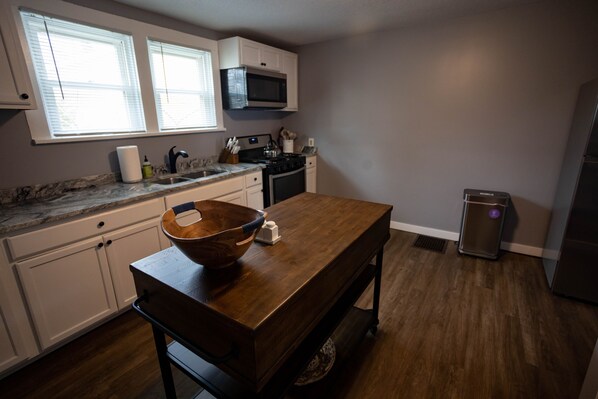 A kitchen with white cabinets, a wooden table, a microwave, and a refrigerator.