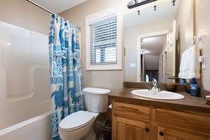 A bathroom with a shower curtain, toilet, sink, and vanity.