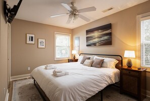 A bedroom with a bed, two bedside tables, a ceiling fan, a window, and artwork on the wall.