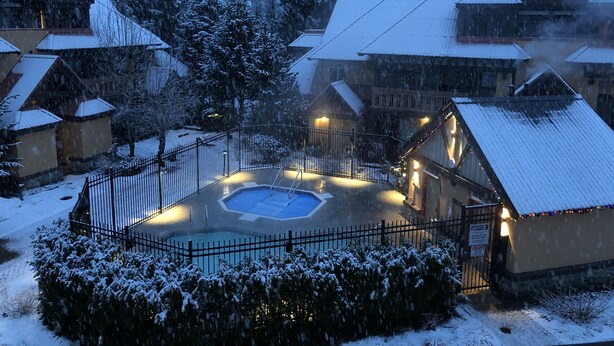 A snow-covered outdoor pool area surrounded by wooden buildings with snow on the roofs.
