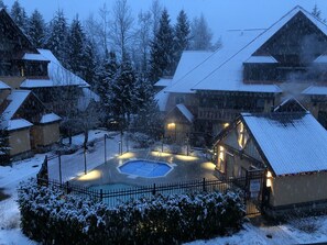 Une piscine extérieure recouverte de neige, entourée de bâtiments en bois dont les toits sont également enneigés.