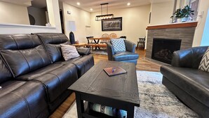 A living room with a leather sofa, a wooden coffee table, a fireplace, and a dining area with a table and chairs.