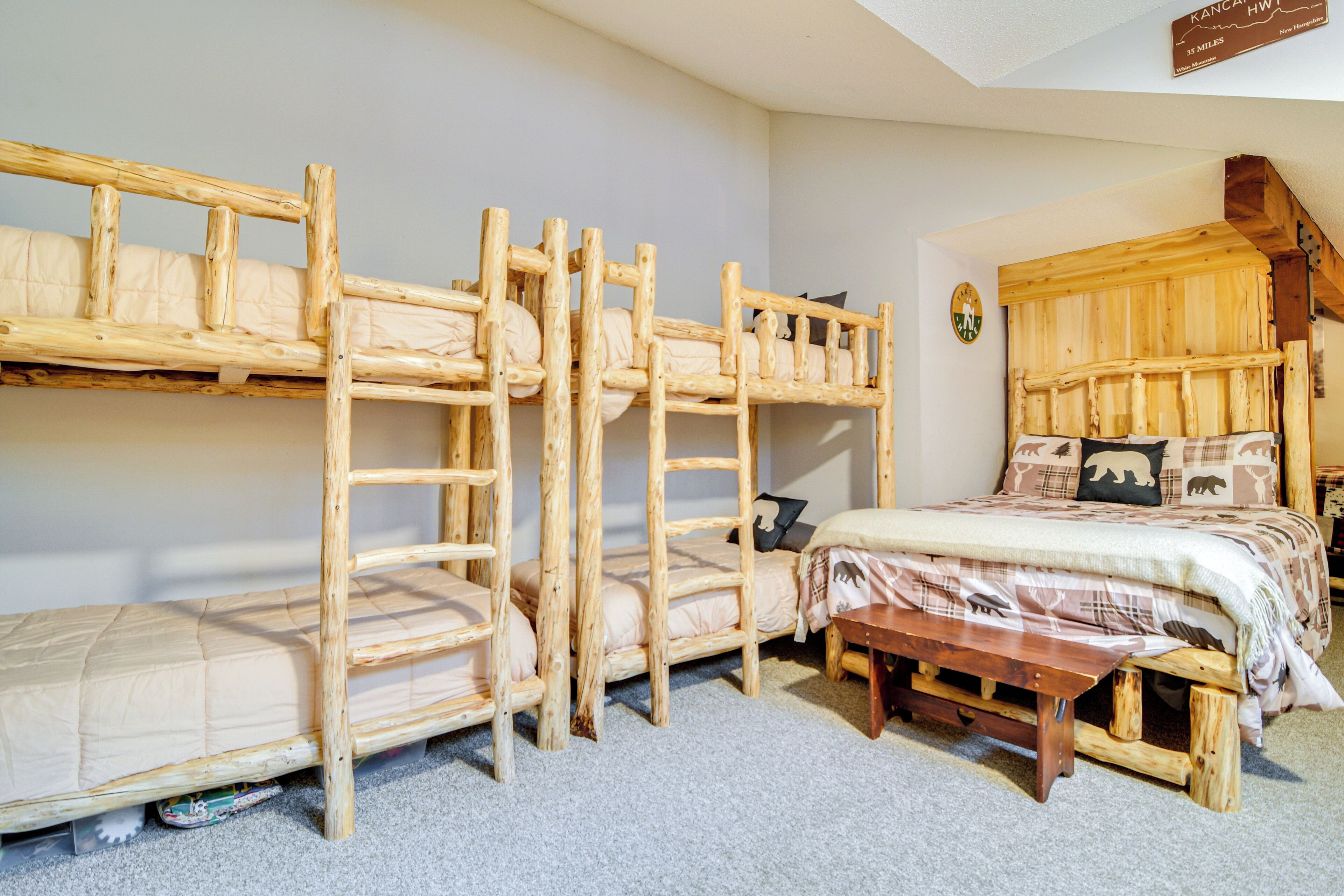 Una habitación con literas, un banco de madera y una cama con colcha estampada.