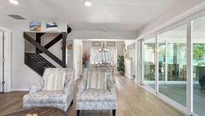 A spacious living room with a modern staircase, a dining area, and large glass doors leading to a balcony.