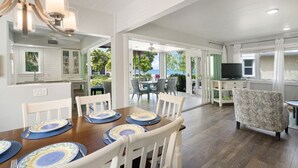 A spacious dining area with a wooden table set for six, a television in the background, and a view of the outdoors.